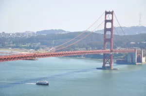 A Red and White Fleet bay cruise boat sailing under the Golden Gate Bridge on a clear day in San Francisco.