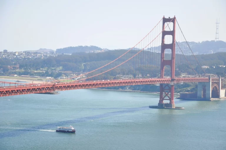 A Red and White Fleet bay cruise boat sailing under the Golden Gate Bridge on a clear day in San Francisco.