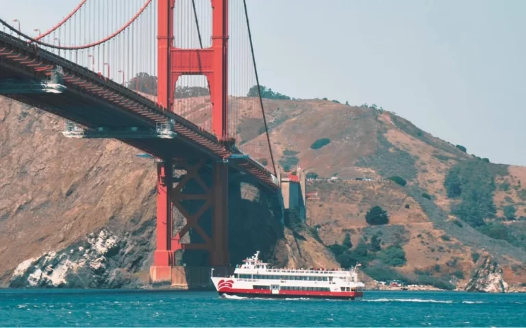 Red and White Fleet bay cruise boat sailing past the Golden Gate Bridge tower in San Francisco.
