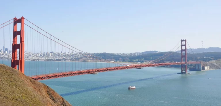 A wide view of the Golden Gate Bridge with a Red and White Fleet boat sailing underneath on the San Francisco Bay.