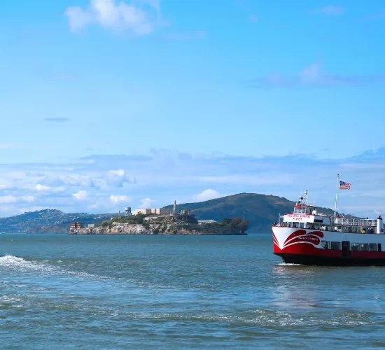 Red and White Fleet bay cruise boat sailing past Alcatraz Island in San Francisco Bay.