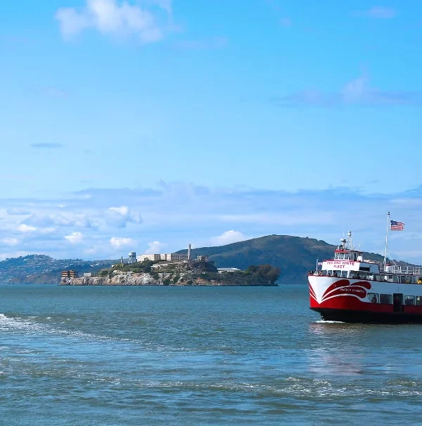 Red and White Fleet bay cruise boat sailing past Alcatraz Island in San Francisco Bay.