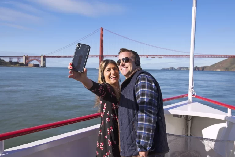 A happy couple taking a selfie on a Red and White Fleet boat with the Golden Gate Bridge in the background.